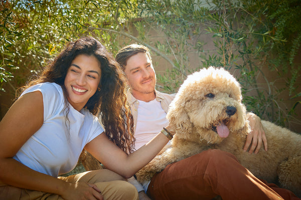 Two owners smiling with their dog in a garden
