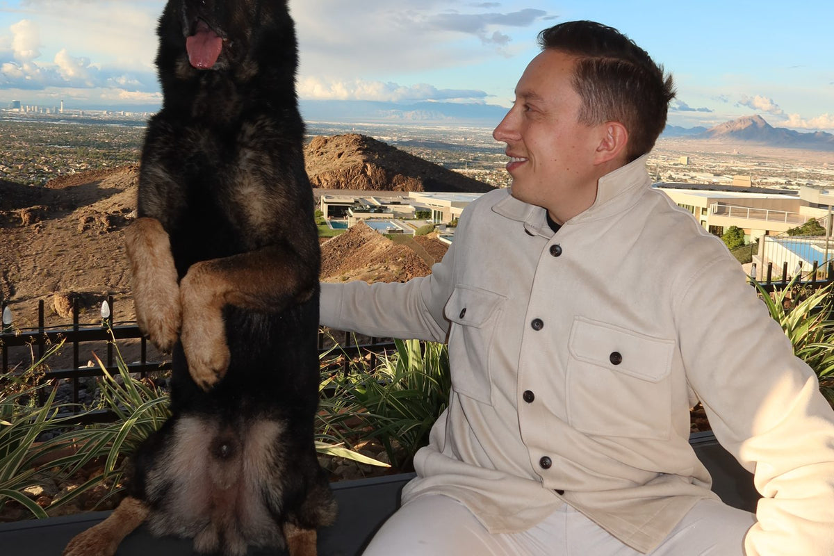 German shepherd sitting beside its handler on a desert overlook